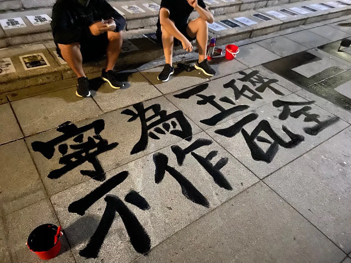 Two people in black sitting beside a slogan on a stone pavement that reads 寧為玉碎，不為瓦全