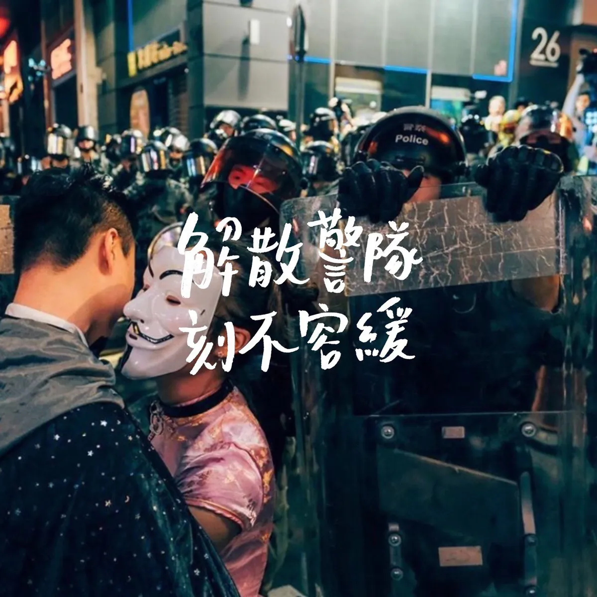 A protester in a Guy Fawkes mask and pink outfit stands face-to-face with a line of riot police holding shields. White text reads 解散警隊，刻不容緩