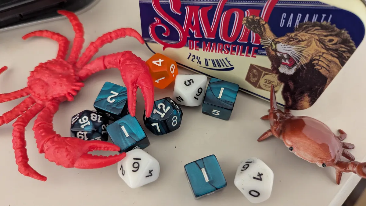 A random assortment of crap on my desk: some toy crabs, a tin of French soap featuring a roaring lion, and a bunch of random dice in dark green, white, and orange