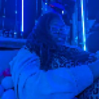 a pixellated, blue-toned picture of a black person with long locs and chunky framed glasses.