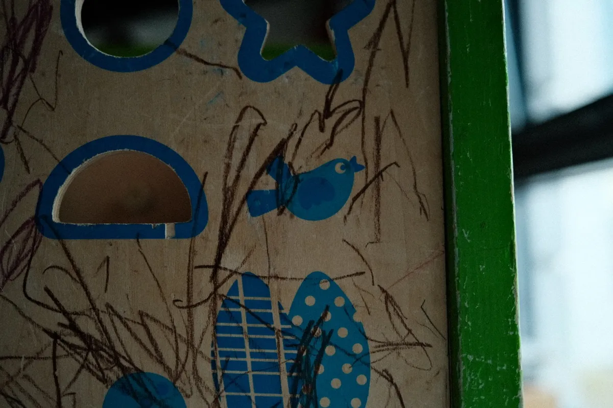 Puzzle piece board featuring blue bird and shapes, with child’s scribbles covering the surface. Set against a wooden background with a green edge, partially shadowed.