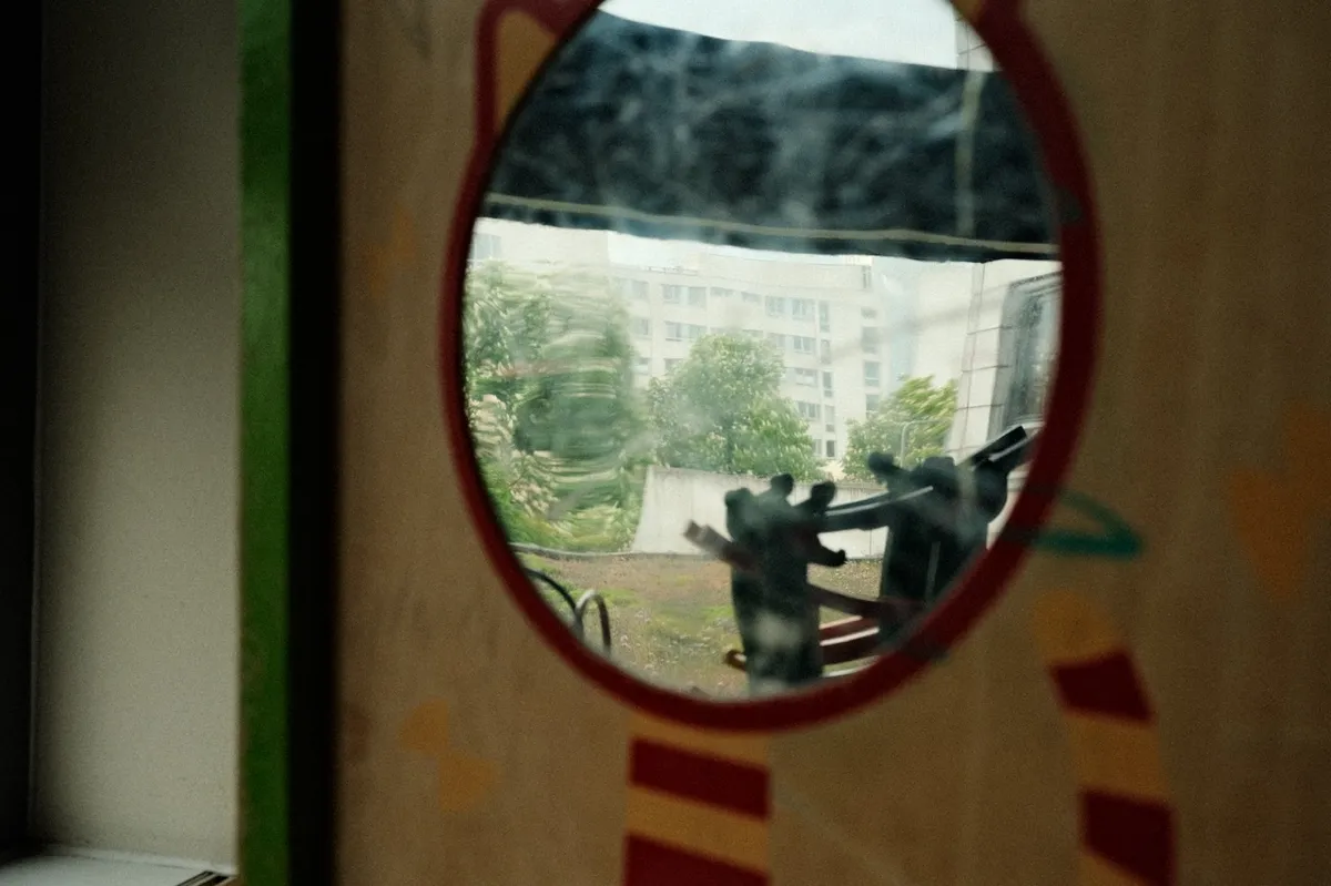 Circular mirror reflects an outdoor scene with blurred greenery and buildings, surrounded by a decorative frame with red and yellow stripes.