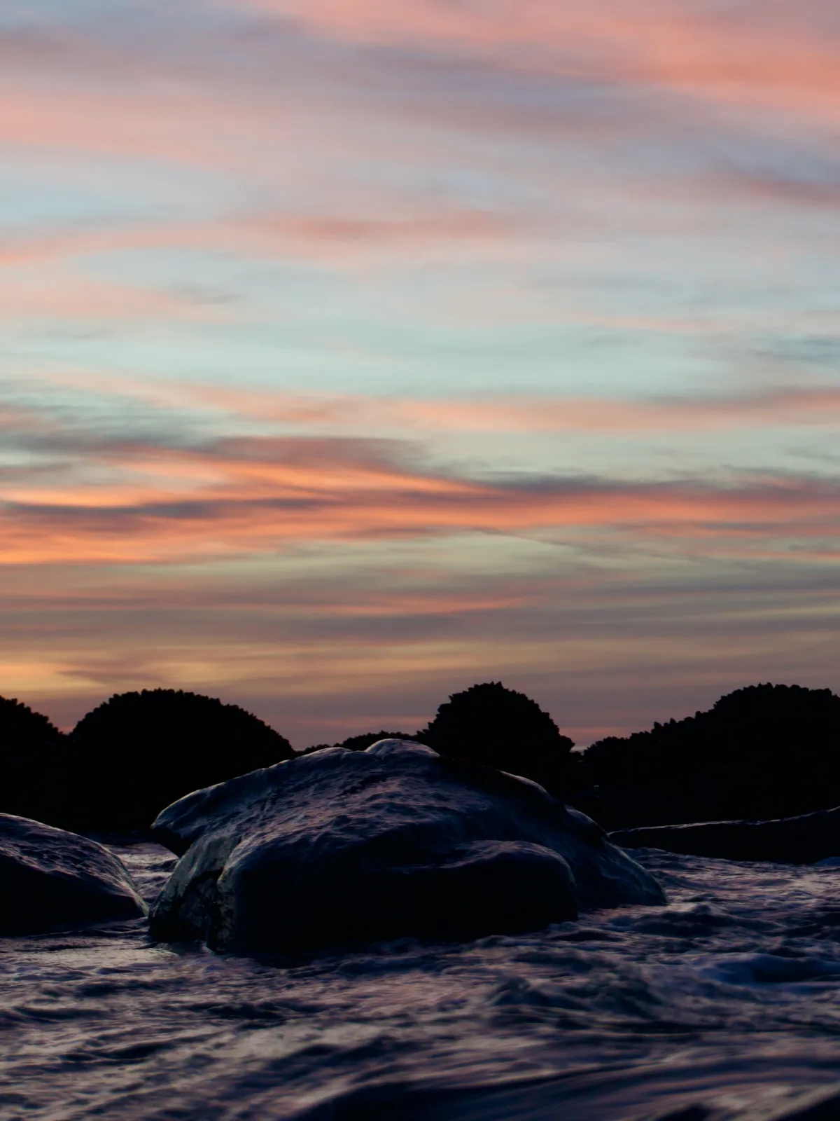 Rock in water below colored clouds