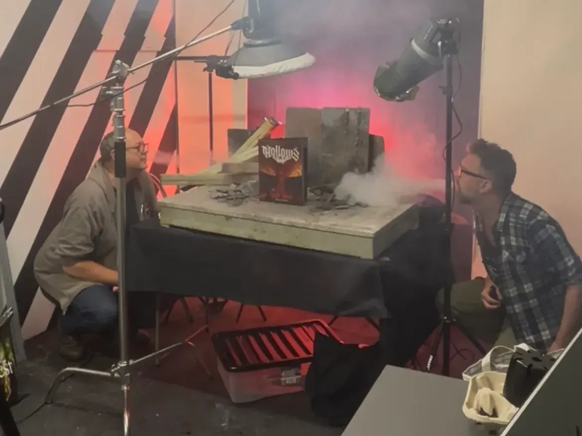 two men kneeling by a table, blowing vape smoke onto a book for a photoshoot