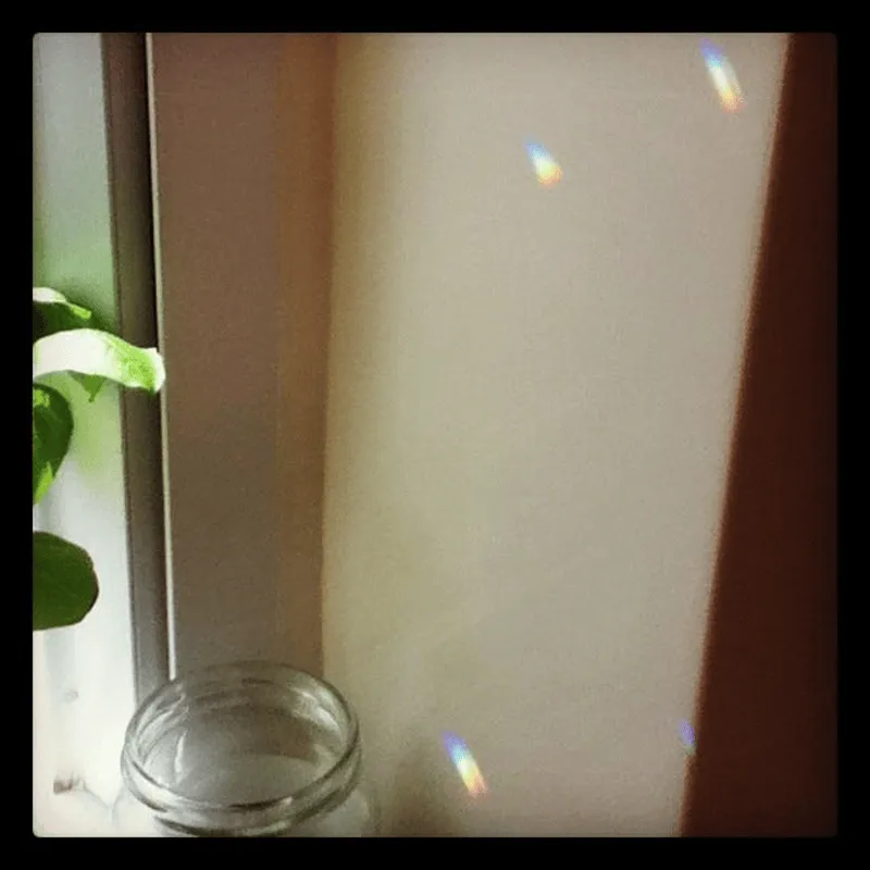 A corner by the window sill with flecks of rainbow light against the blank, cream-colored wall.