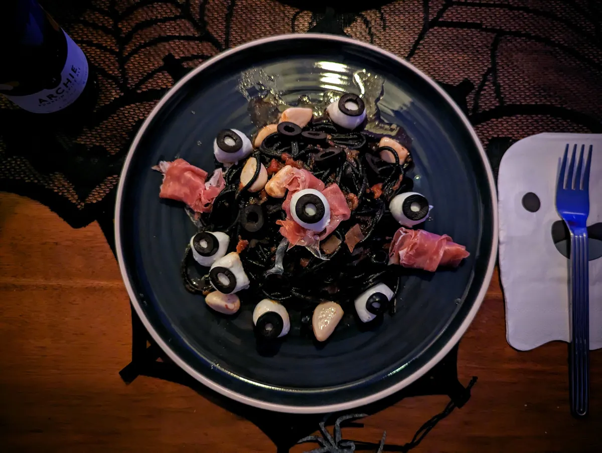 A plate of squid ink pasta with "eyeballs" made of mozzarella balls and sliced black olives.