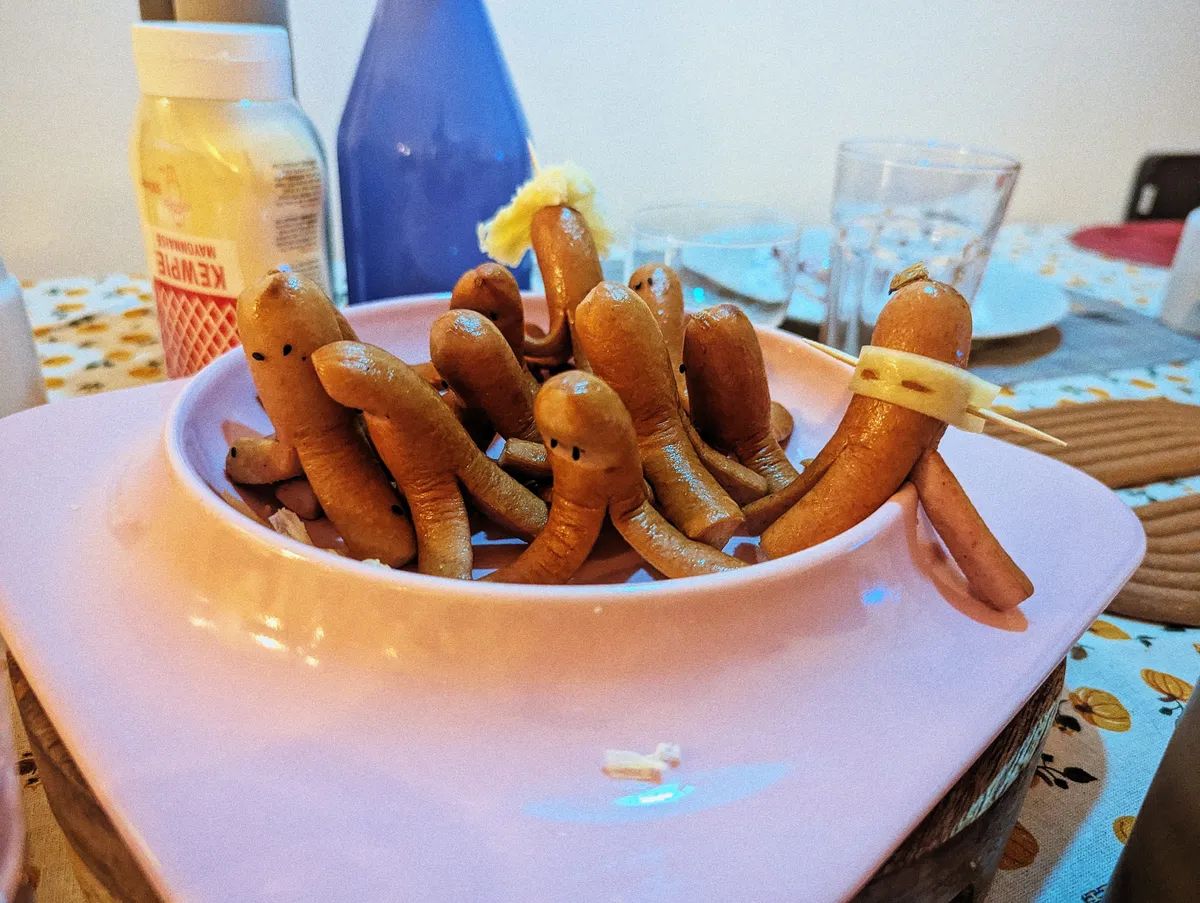 A pink plate filled with hotdogs that have been cut to look like octopuses. One octodog is wearing a ninja mask made of cheese, leaning with one "tentacle" outside of the plate.