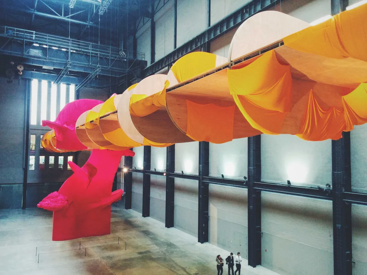 A large exhibit constructed inside the main hall. There is a large pink structure, with giant swirls covered in yellow cloth (almost looks like a drill).