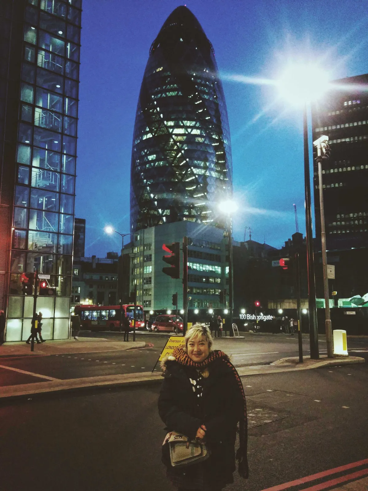 Peige, with blonde hair, stands in front of the Gherkin wearing a knitted tiger scarf.