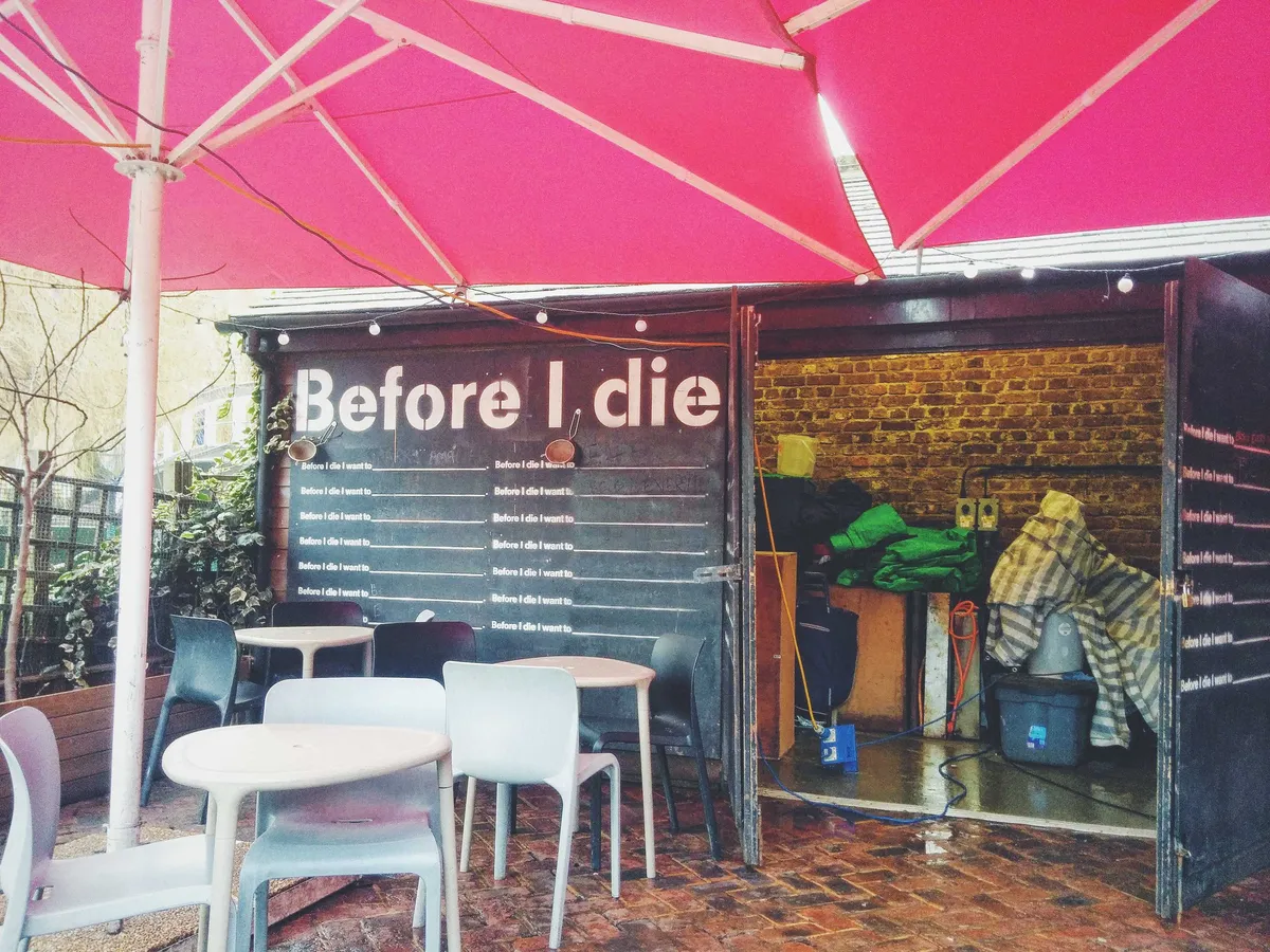 A container with the words "Before I die" spraypainted on it. Beneath are two columns with the words, "Before I die I want to _______."