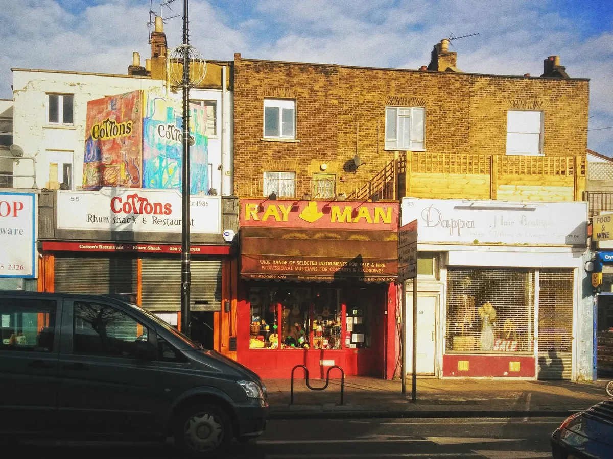 A shop painted bright red stands out amongst a row of other shops. The sign says "Ray Man" in yellow.