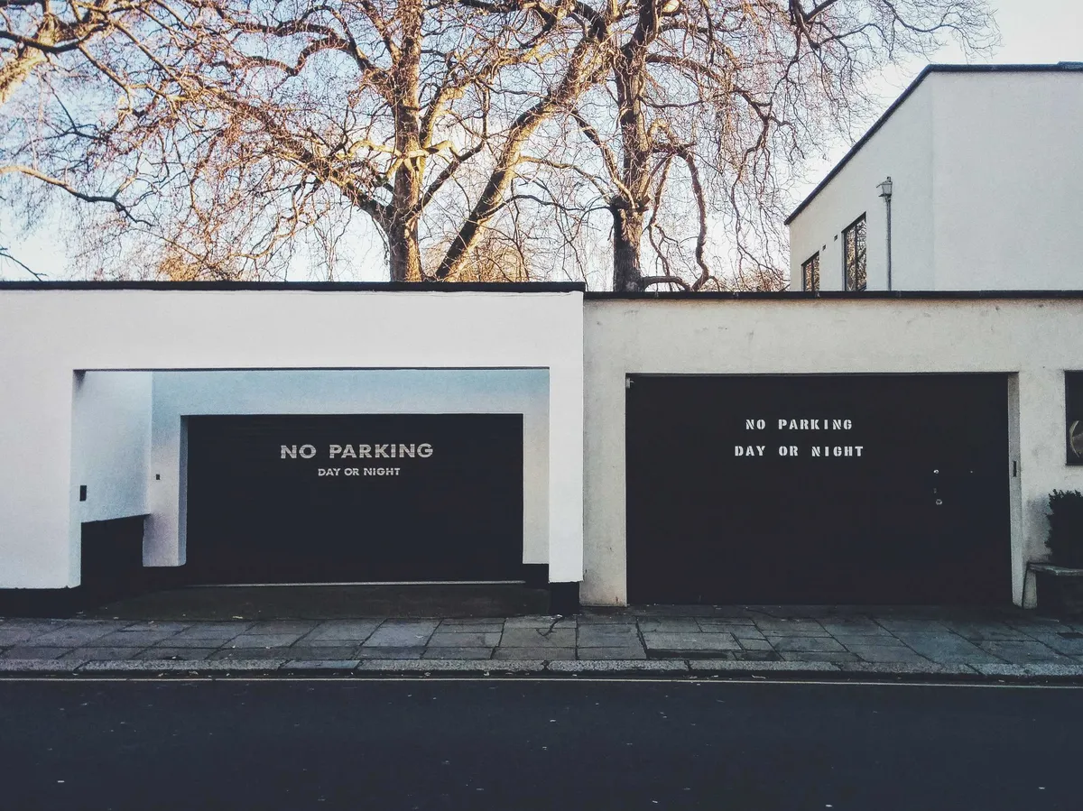 Two garage doors painted black against a white structure. Both have signs in different fonts that say, 