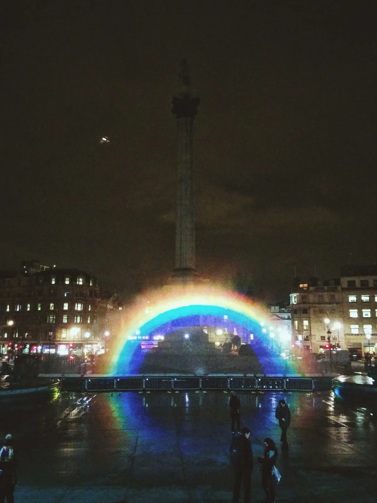 A rainbow lit up within the water fountain at night, in the middle of Trafalgar Square.