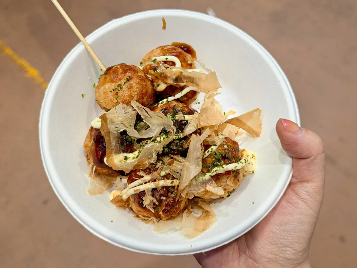 Peige holds a paper bowl with fried balls topped with benito flakes and furikake, drizzled in mayo.