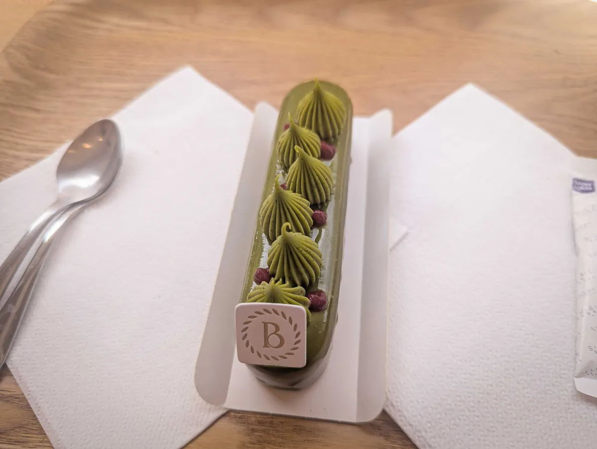 A small oblong-shaped cake that is matcha green, decorated with matcha frosting and tiny chocolate pearls.