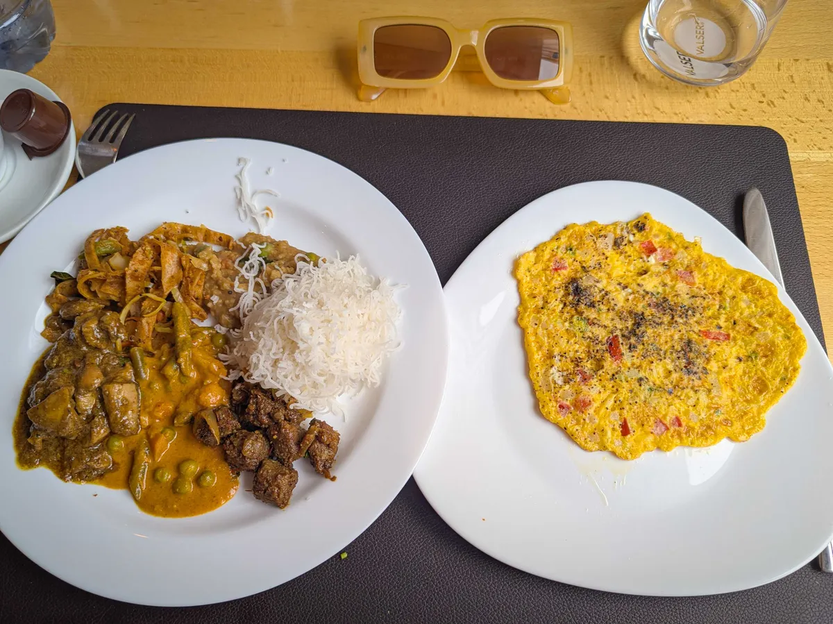 One plate filled with brown-colored food and rice, the other plate has an omelette with some slice tomatoes and pepper.