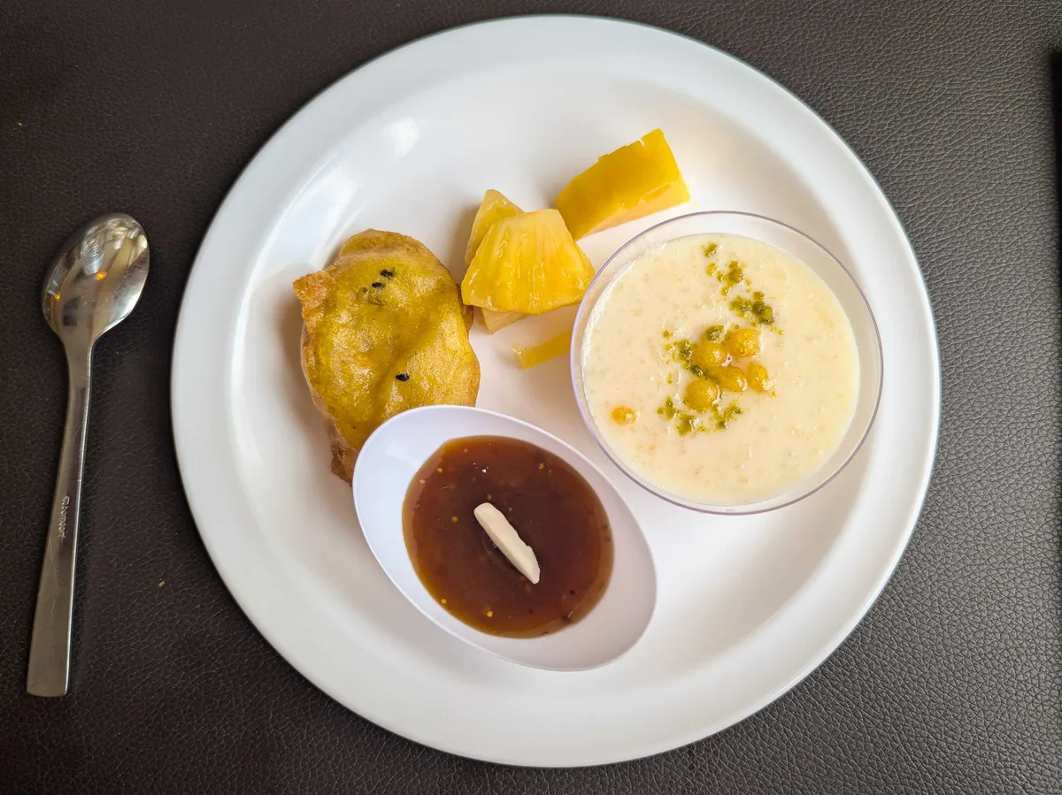 A plate of desserts, including two types of puddings, slices of pineapple, and a fried item.