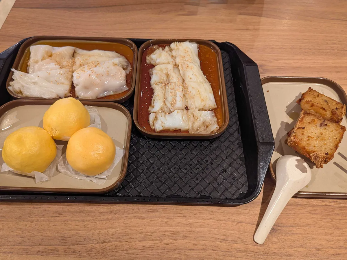 4 small platters containing various dim sum, including custard buns, fried turnip cakes, and two types of chong fun.