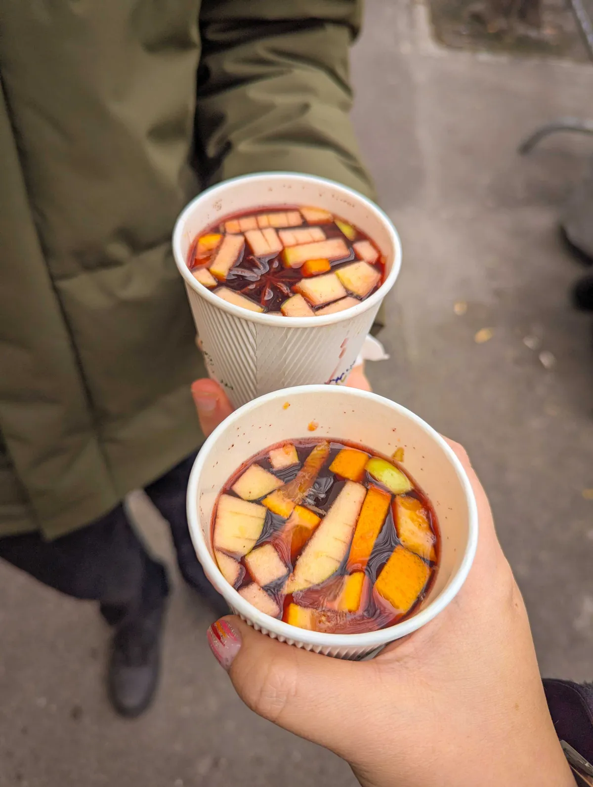 Daniel and Peige toast two cups of hot dark red punch, filled with sliced fruit and a star of anis.