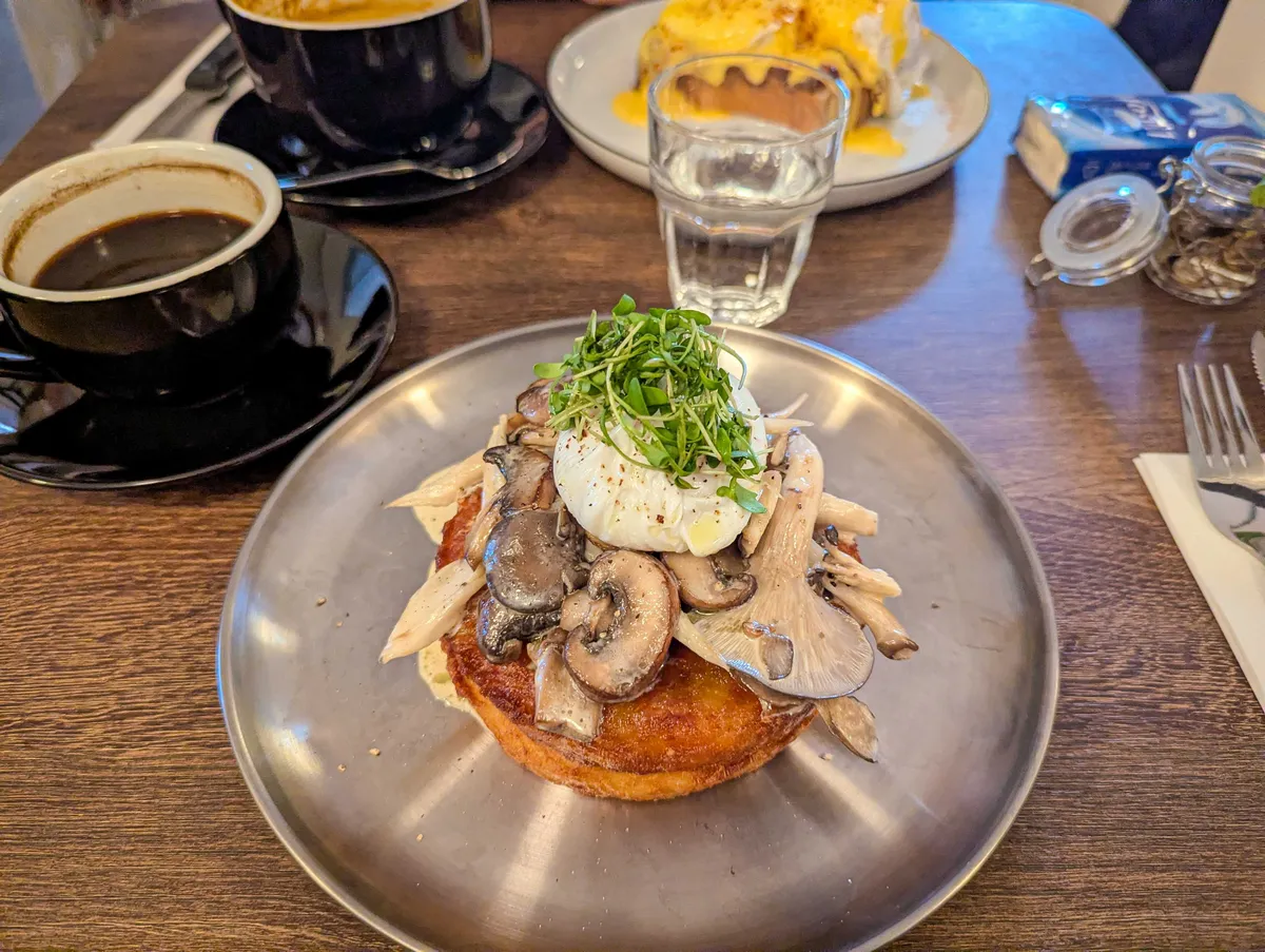 A heap of of sliced mushrooms piled on top of a seemingly small but thick slice of rösti. There's also a poached egg on top with microgreens.