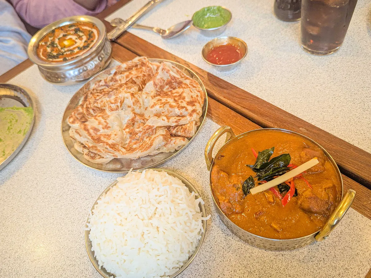 A large plate of roti, a bowl of rice, and two orange-colored curries in ornate dishes.