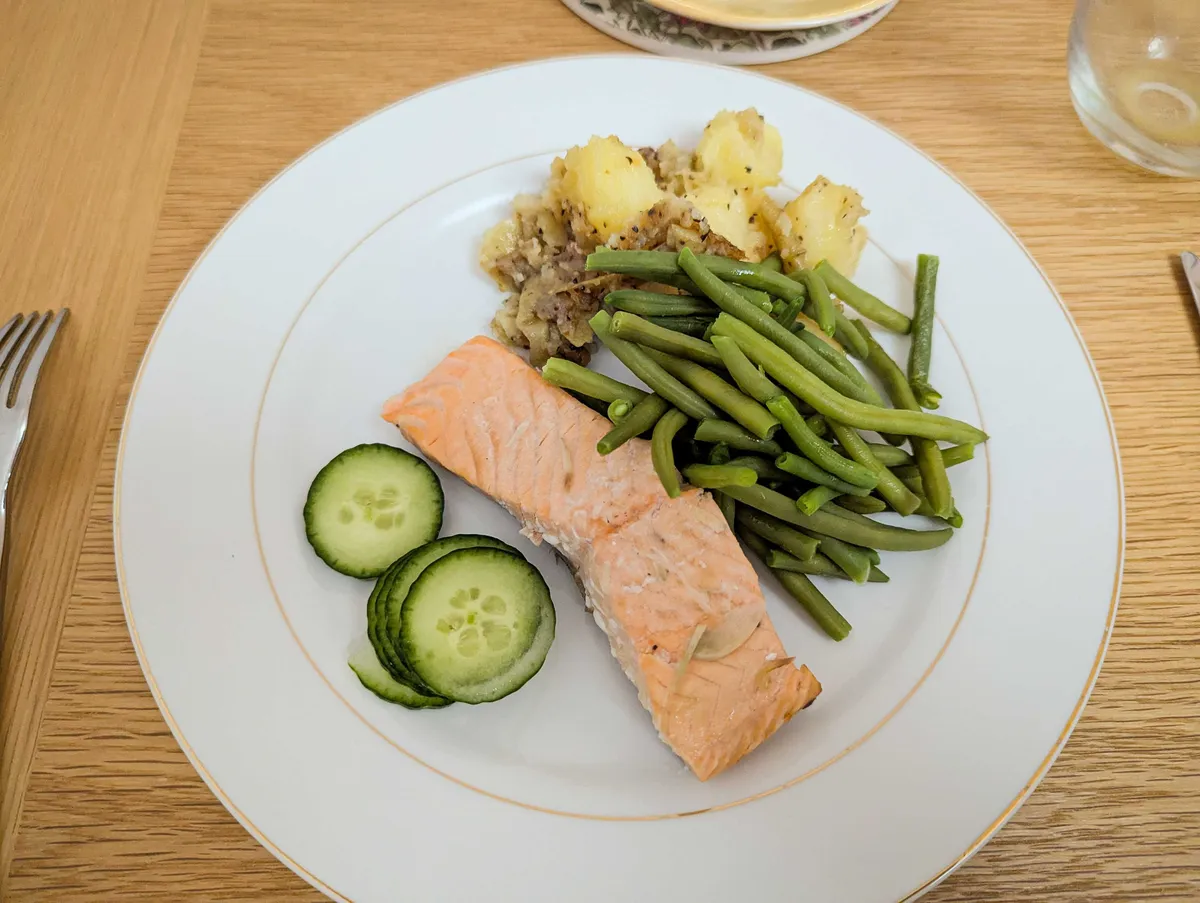Salmon, green beans, potatoes, and cucumbers on a white plate.