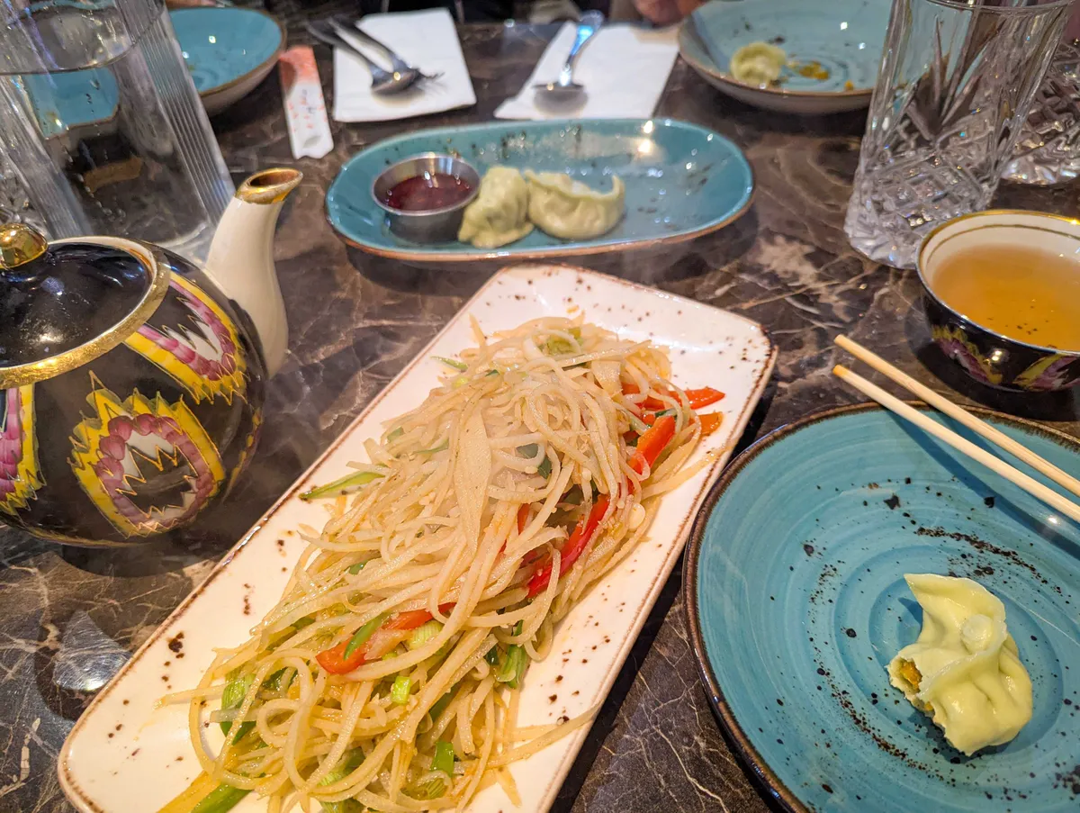 A long plate of stir-fried potatoes with bell peppers. Half-eaten dumplings can be seen across various plates.