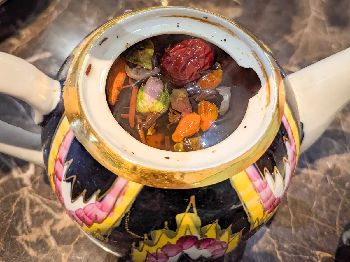 An uncovered tea pot with goji berries, dates, and flowers steeping in the tea.