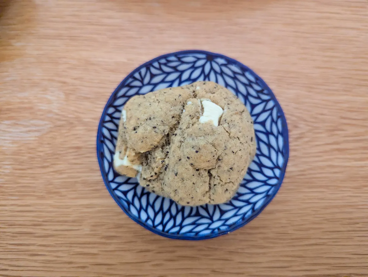 A small, round beige cookie with some white chocolate and tiny black dots sprinkled throughout.