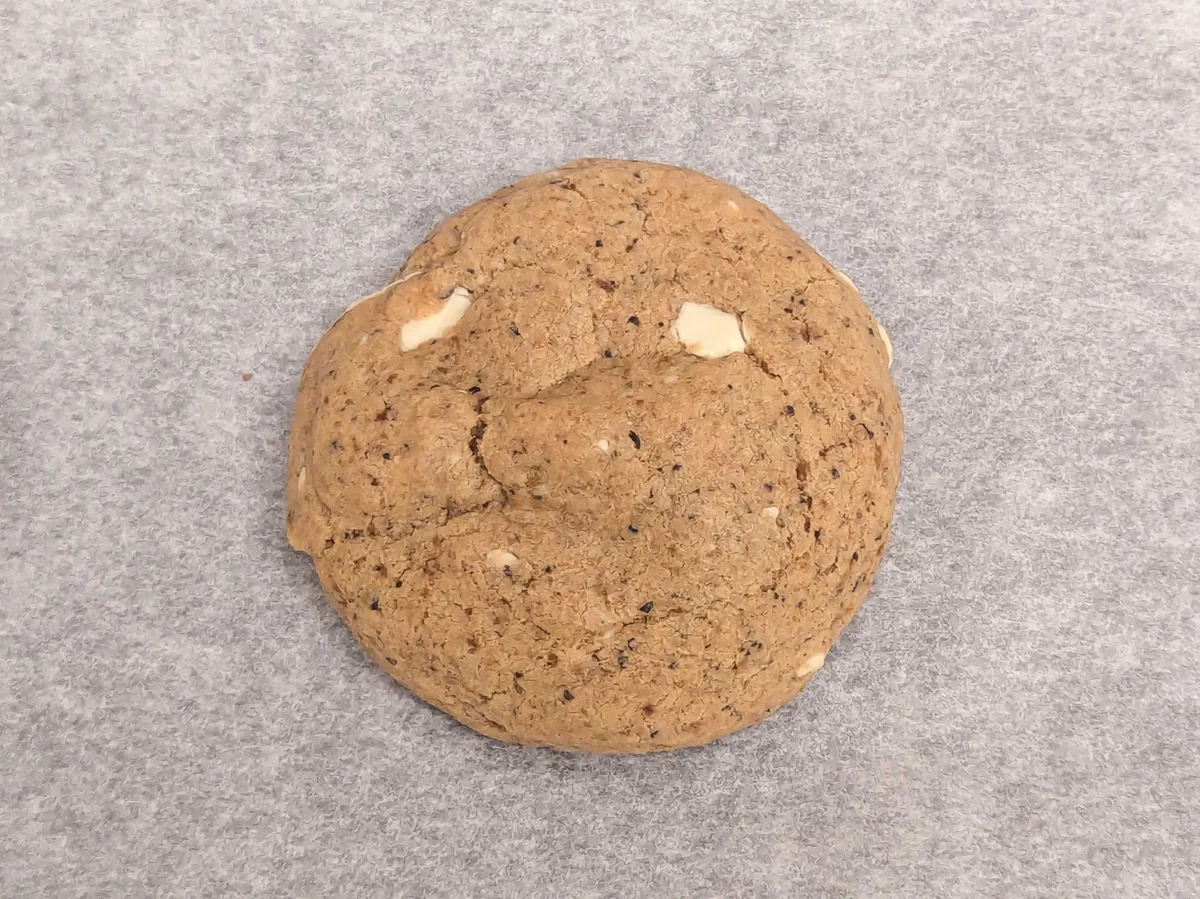 Close-up of the earl grey cookie. It is a good, round shape. There are some white chocolate bits peaking out. Bits of earl grey tea leaves, ground to bits, are flecked throughout the dough.