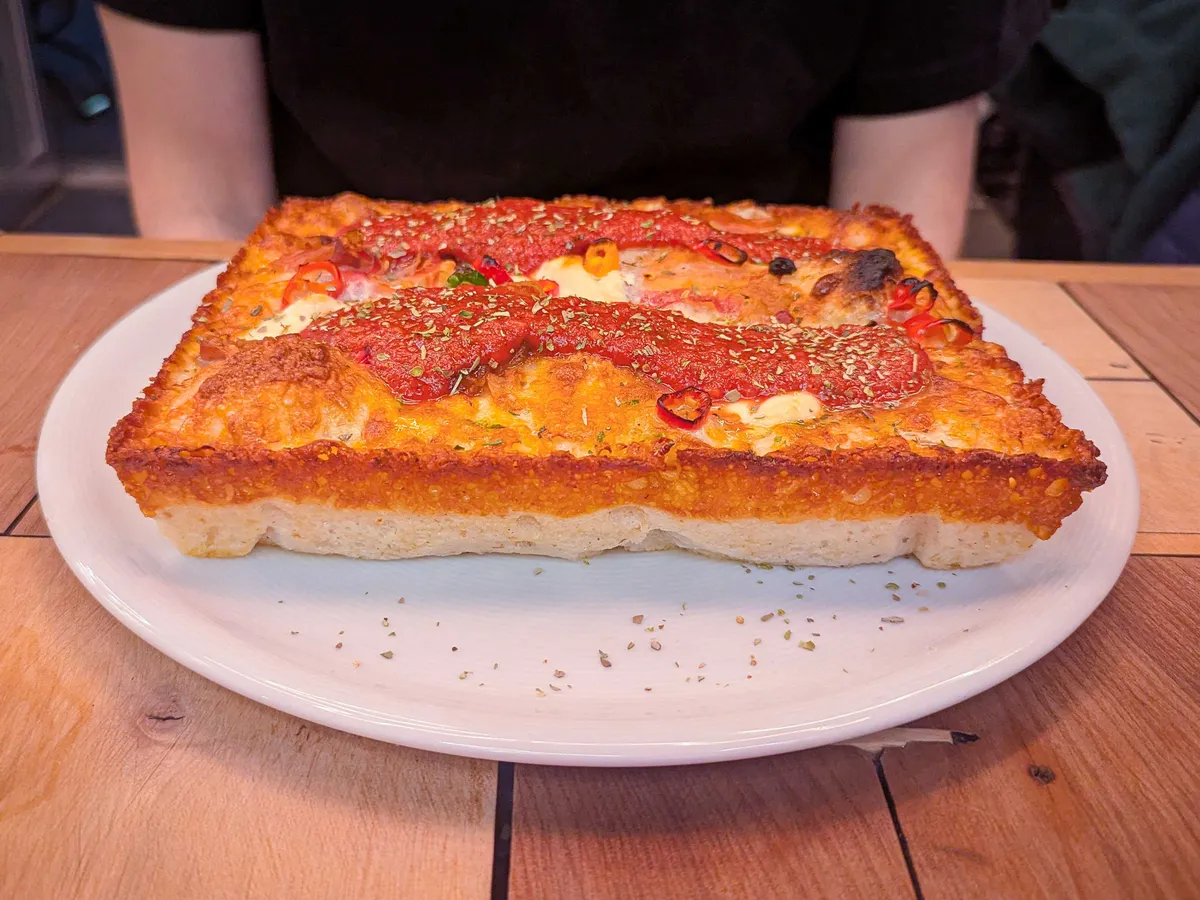 A rectangular shaped pizza that is about 2 inches thick. There is tomato sugo on top and cheese.