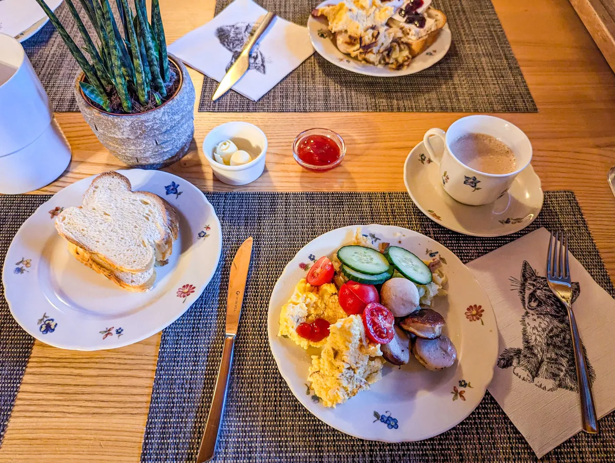 A breakfast spread with a plate of scrambled eggs, sausages, and veggies, and another plate of sliced bread.
