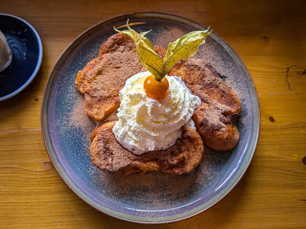 A plate of cinnamon french toast with whipped cream and a single sea buckthorn as garnish.