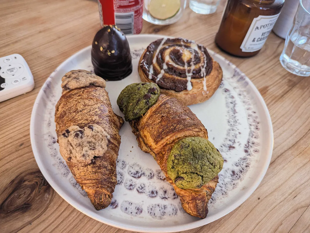 A plate with two crookies, a cinnamon bun, and a chocolate cream puff.
