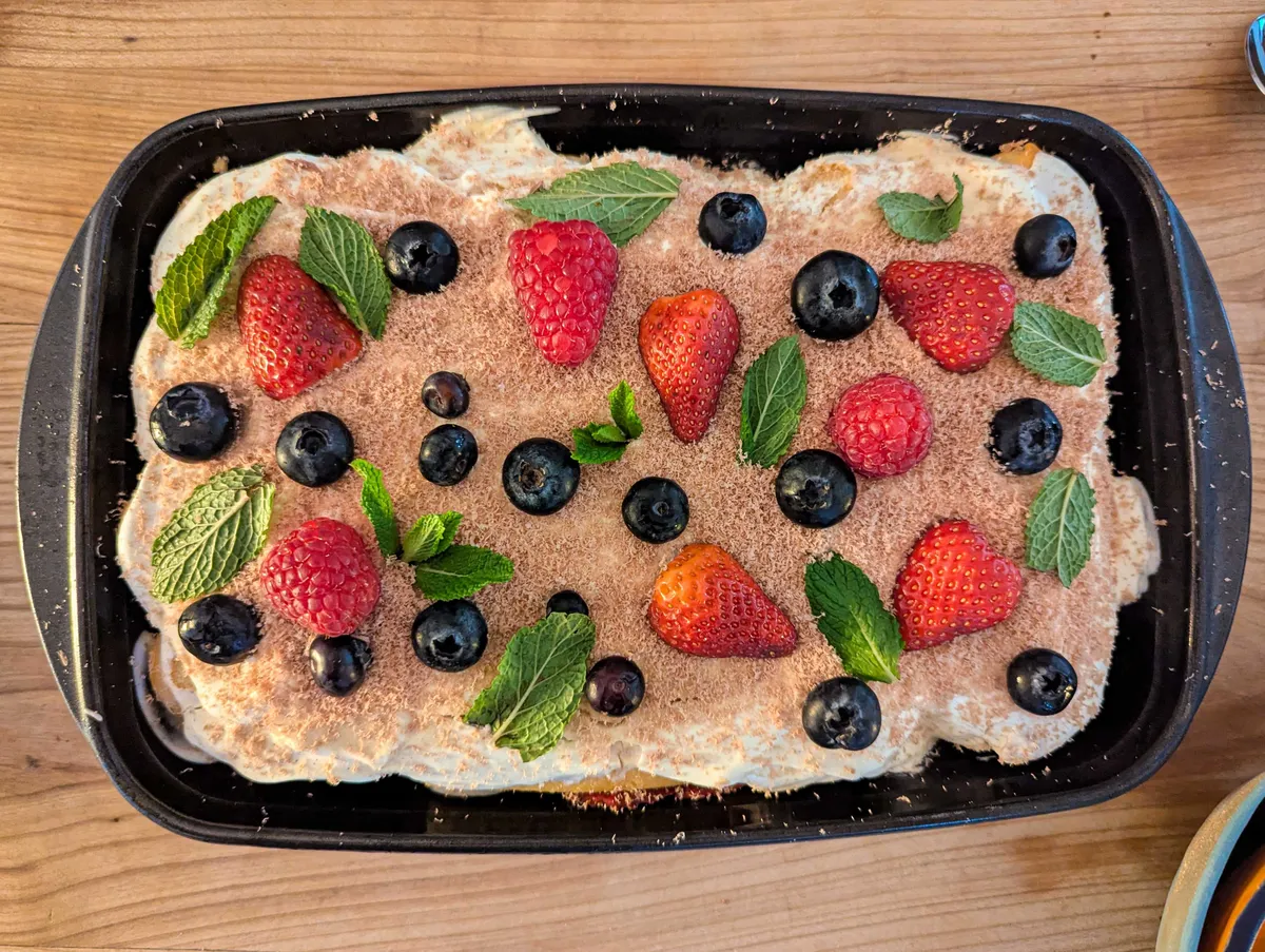 A rectangular baking tray containing a whipped cake covered in berries.