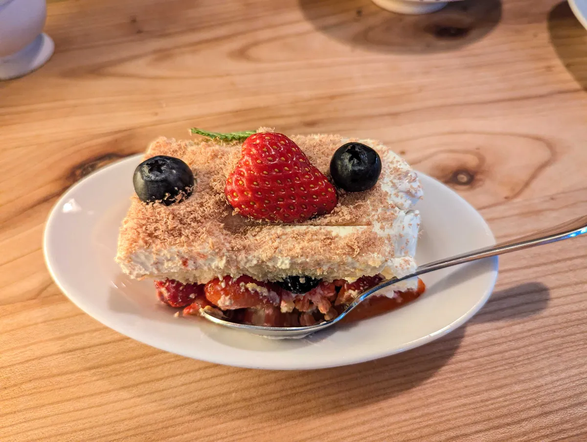 A slice of cake. There are strawberries oozing from the bottom.