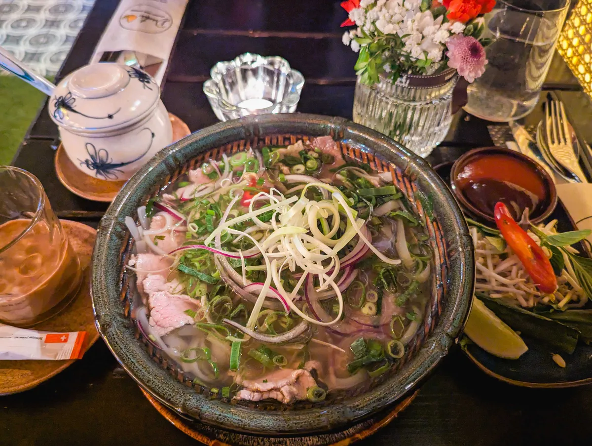 A bowl of pho garnished generously with three kinds of onions and lots of beef.