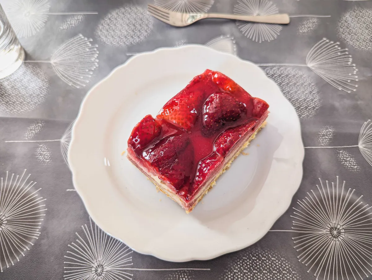 A white plate with a rectangular slice of cake topped with fresh strawberries.