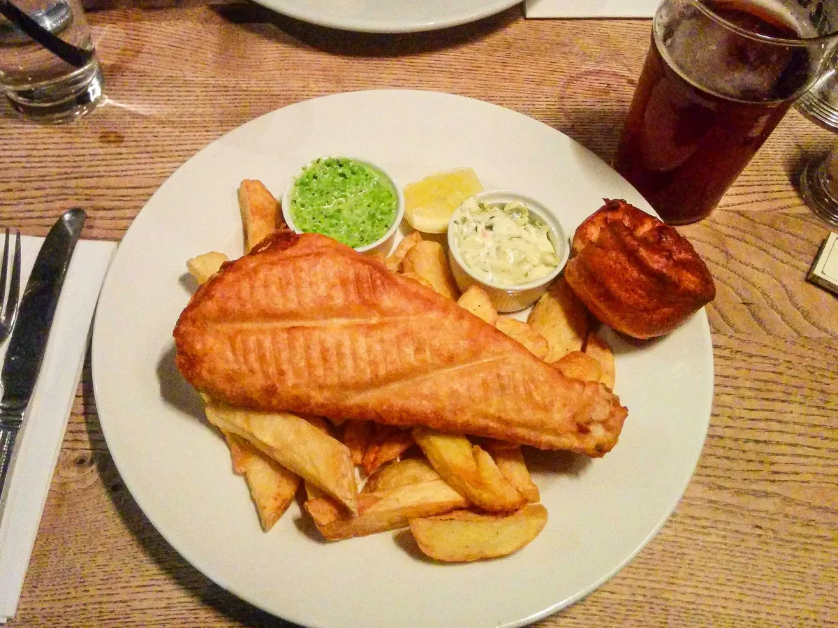 A plate of fish and chips with dipping sauces.