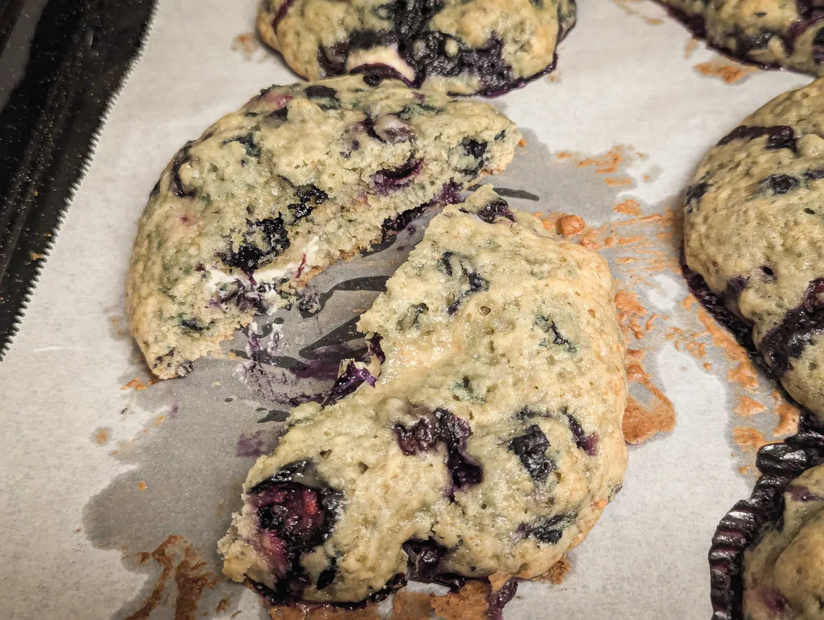 A sliced open cookie revealing some melted cream cheese and oozing blueberry.