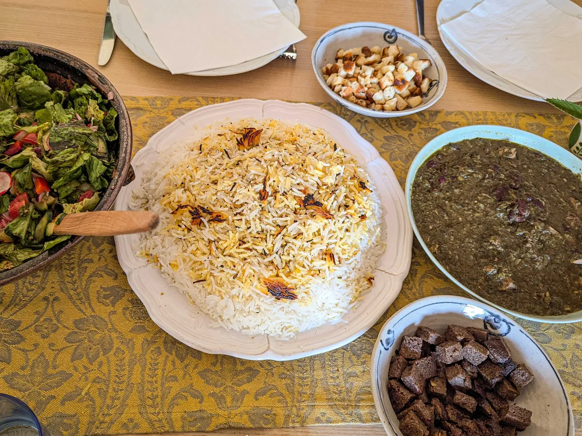 Persian rice on a plate, next to salad and ghormeh sabzi.