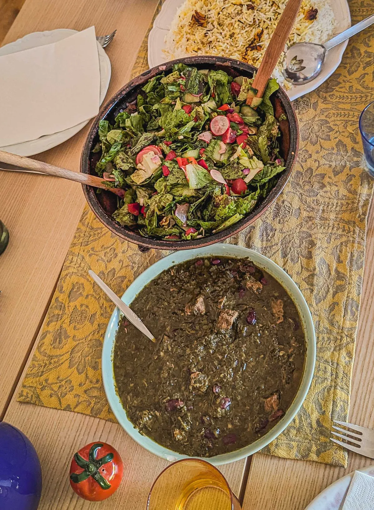 Ghormeh sabzi with visible chunks of meat and red beans, and a large bowl of salad.