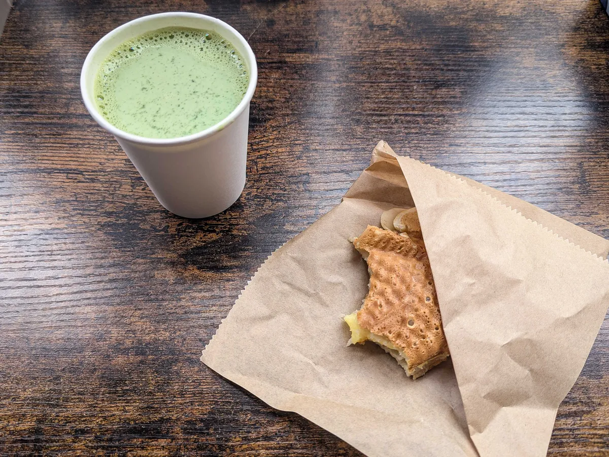 A half-eaten taiyaki inside a brown paper bag and a cup of matcha latte.