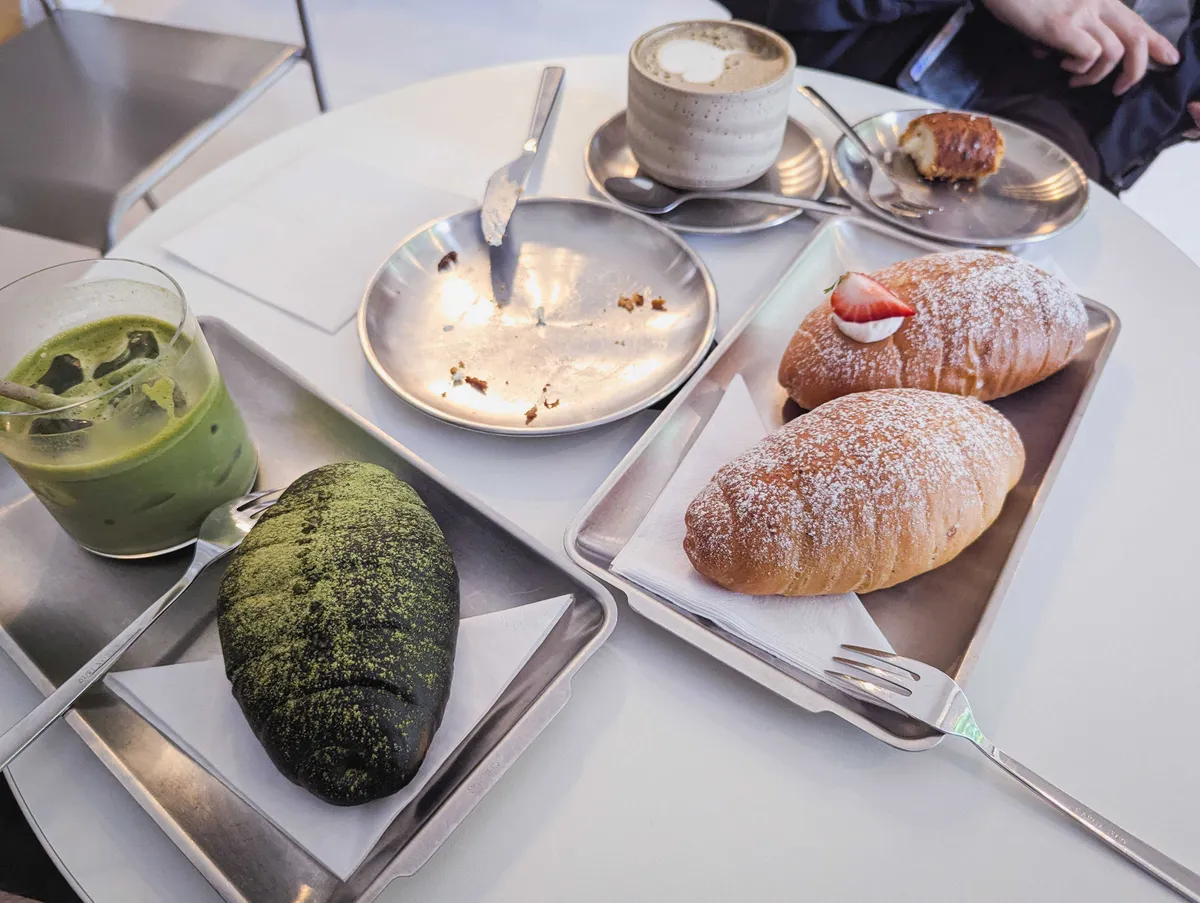 3 salt breads on stainless steal trays, one glass of iced matcha latte and a mug of hojicha latte.