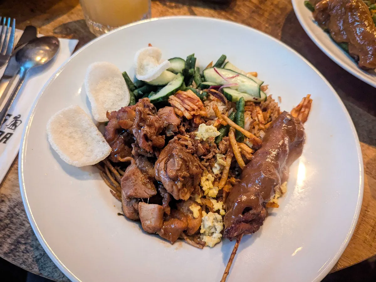 A plate of satay chicken, beef and chicken pieces, with noodles hidden underneath.