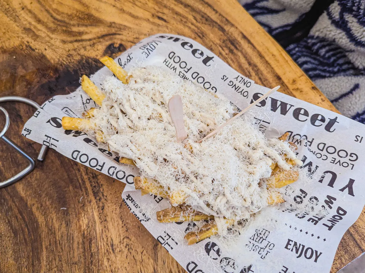 Fries with a thick layer of mayonnaise and finely shredded cheese are served on fake newspaper.
