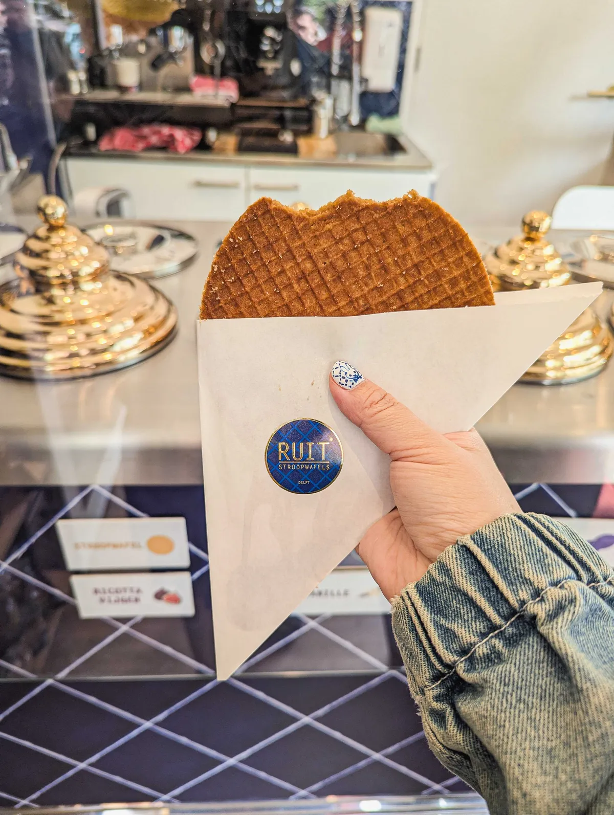 Peige holding a large stroopwafel that's inside a triangular paper bag with the shop's logo on it.