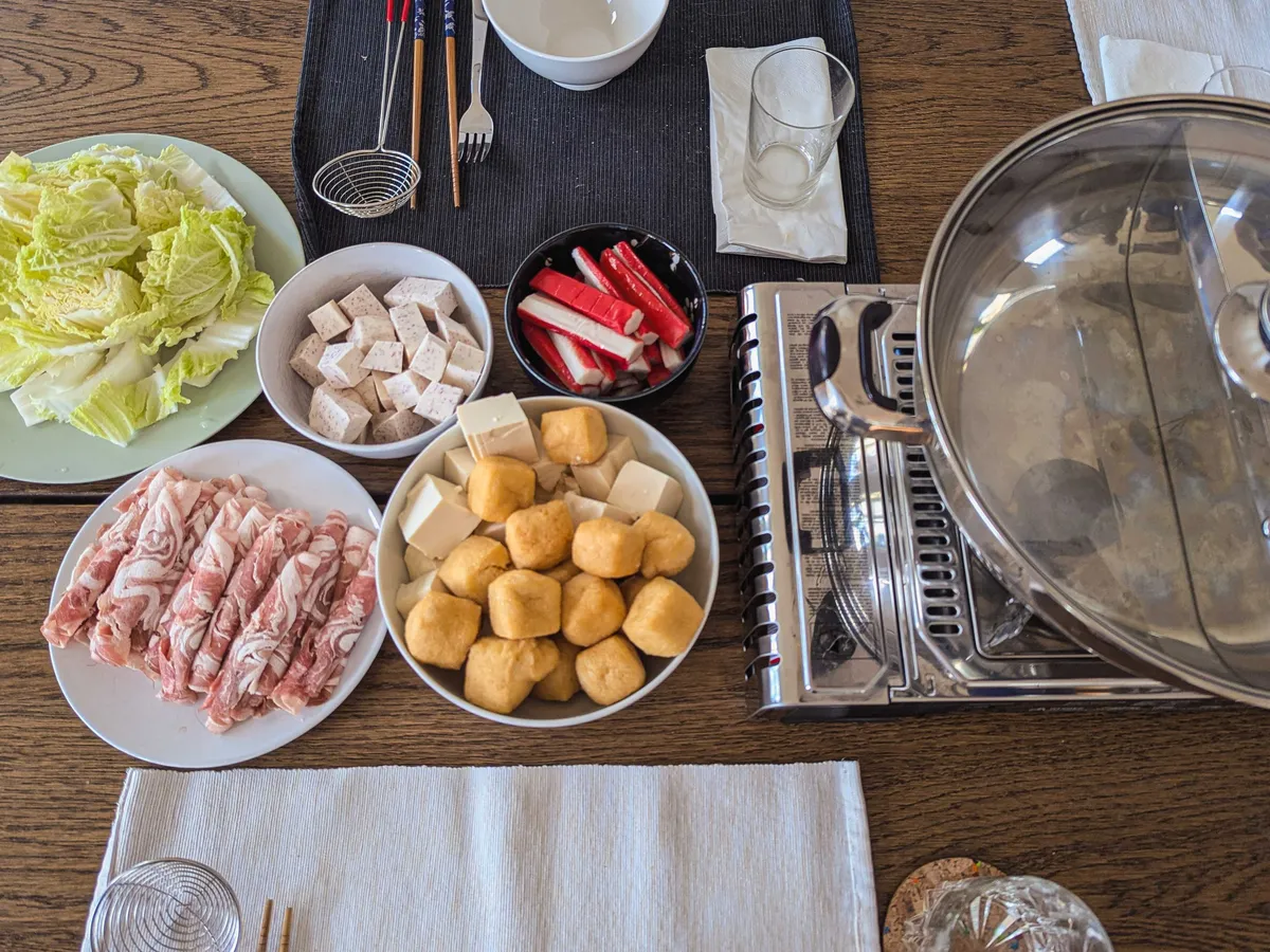 Plates of hot pot ingredients, including Napa cabbage, lamb slices, tofu, and fake crab rolls.