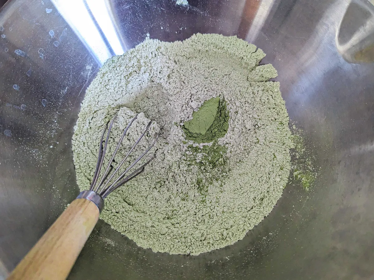 Dry ingredients, including matcha powder, inside a stainless steel bowl.