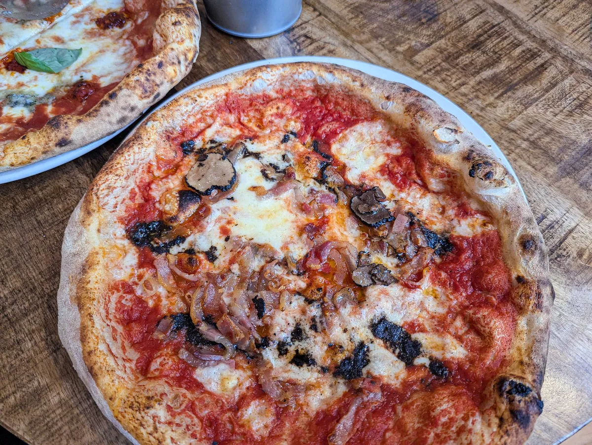 A napoli-style pizza with truffles, thinly sliced bacon, and caramelized onion.